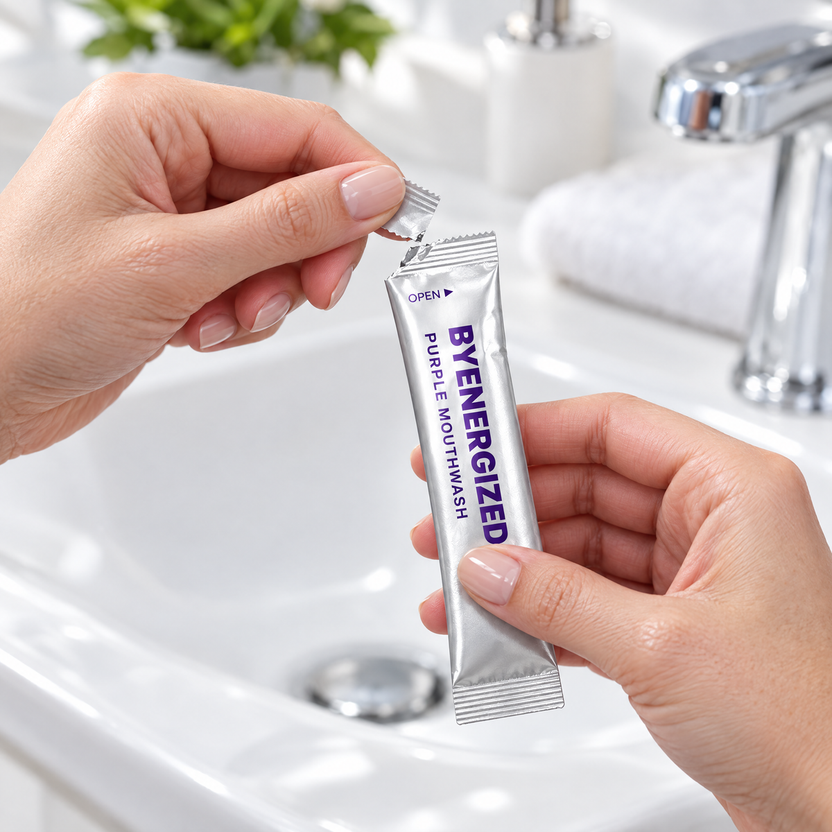 Hands tearing open a Byenergized single-use mouthwash sachet over a bathroom sink