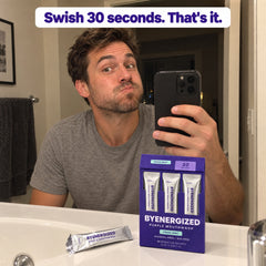Man swishing Byenergized purple mouthwash at the mirror